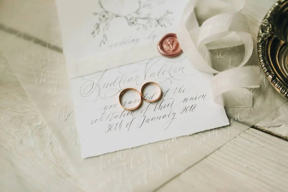 Trouwringen op een handgeschreven uitnodiging met zegel en lint