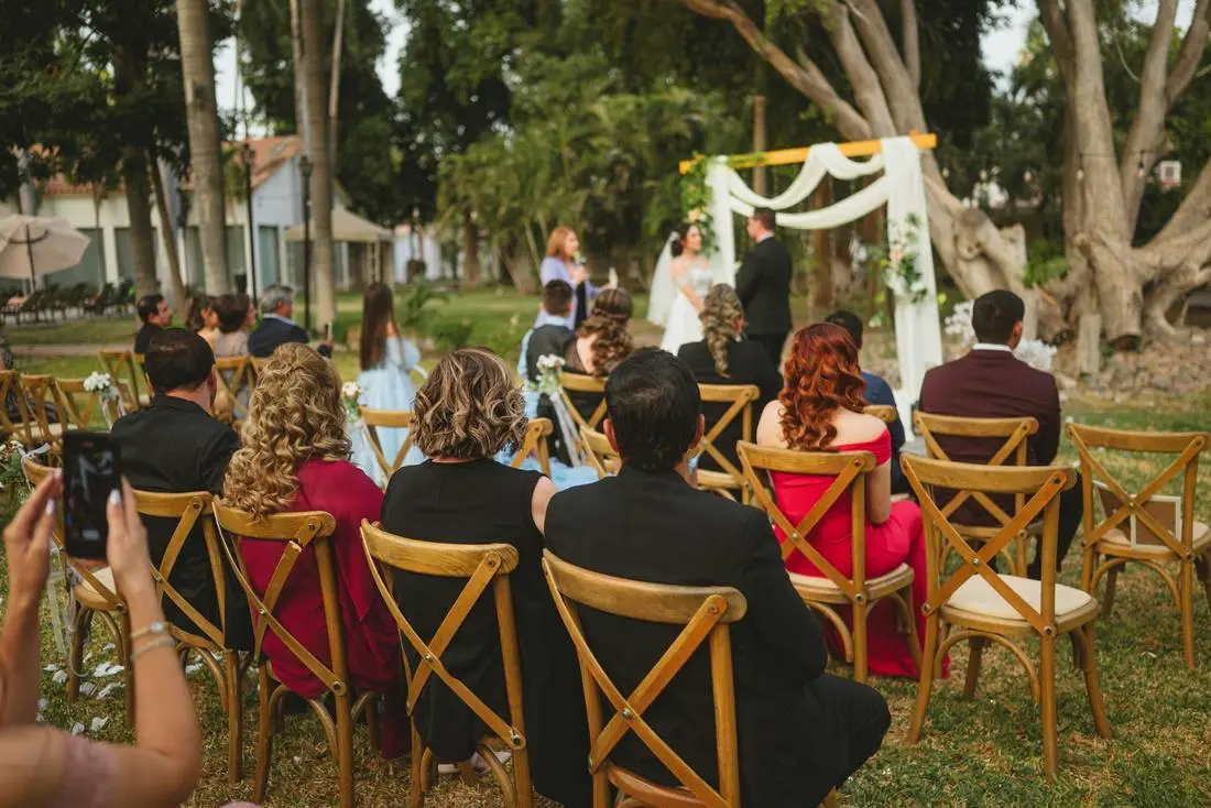 Buitenceremonie met houten stoelen en een boog met witte stof